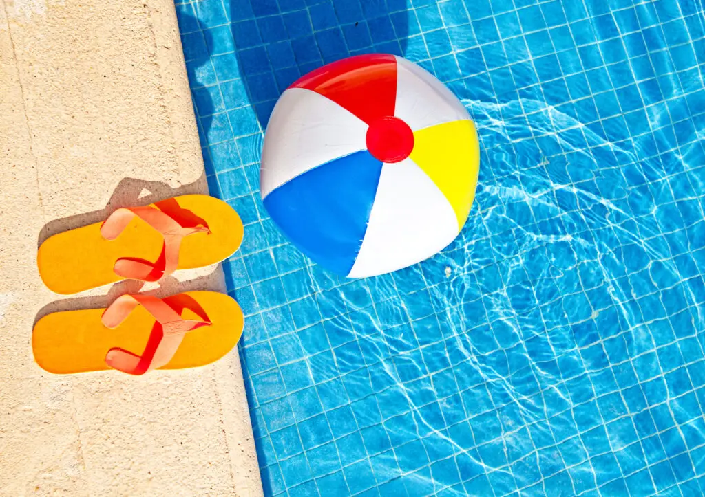 A swimming pool with an inflatable beach ball and orange flip flops