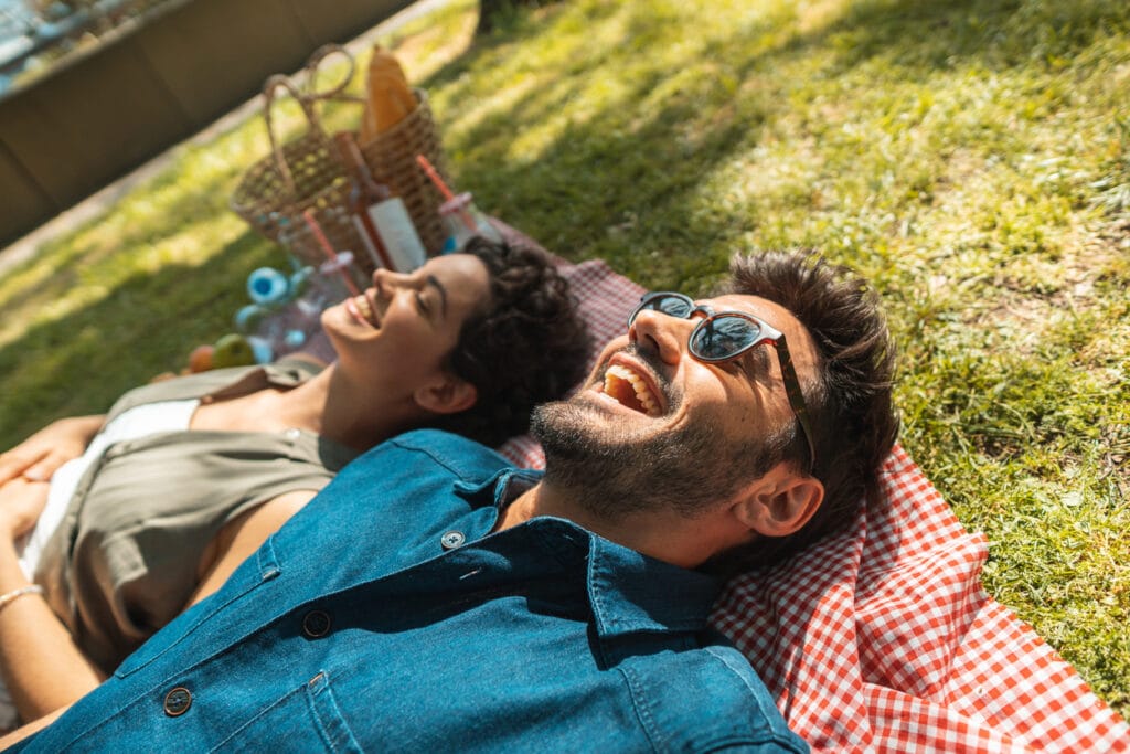 a man and a woman resting on a picnic blanket and looking at the sky