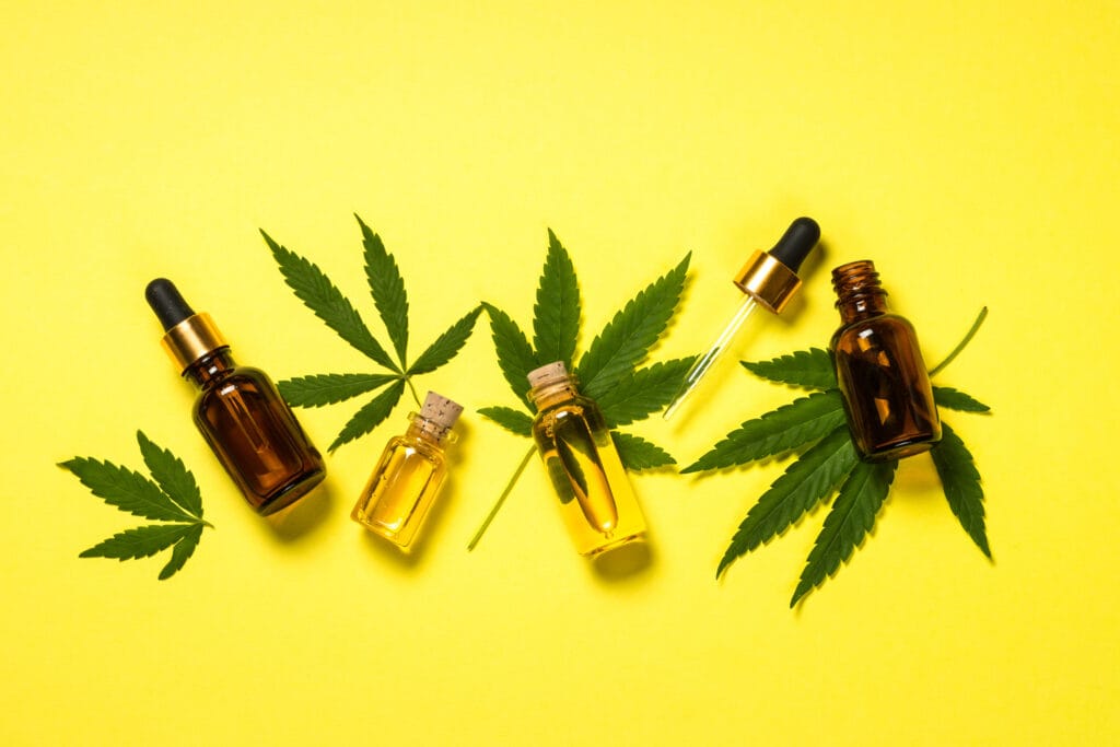 three cannabis tincture bottles and cannabis leaves on a yellow background